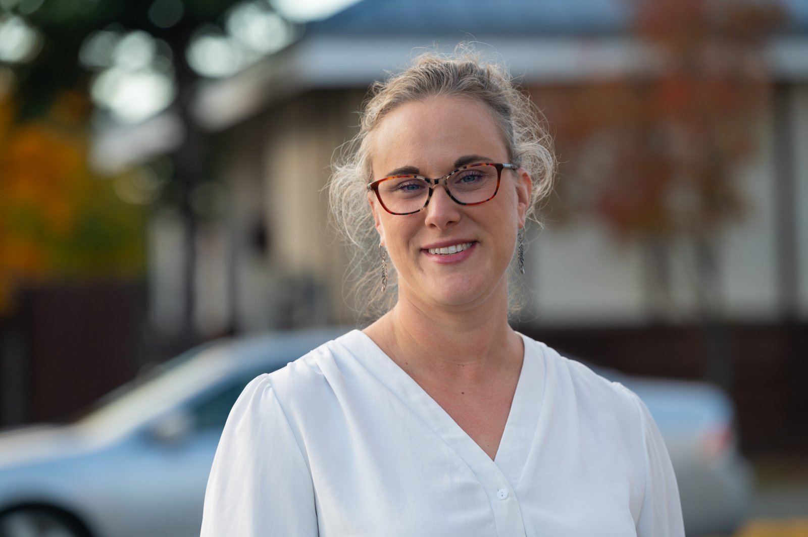 A woman with a white shirt and glasses stands outside.