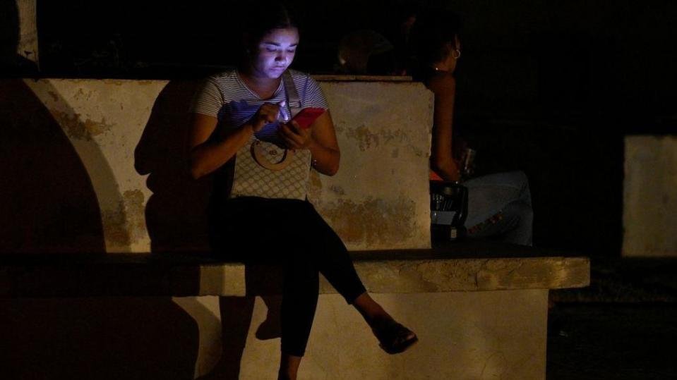 A woman is lit by her mobile phone during the third night of a nationwide blackout in Havana October 20, 2024. 