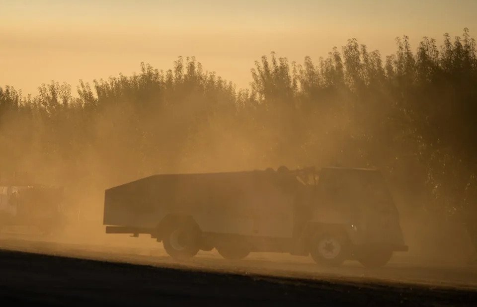 An agricultural truck kicks up dust in an orchard in Cantua Creek.