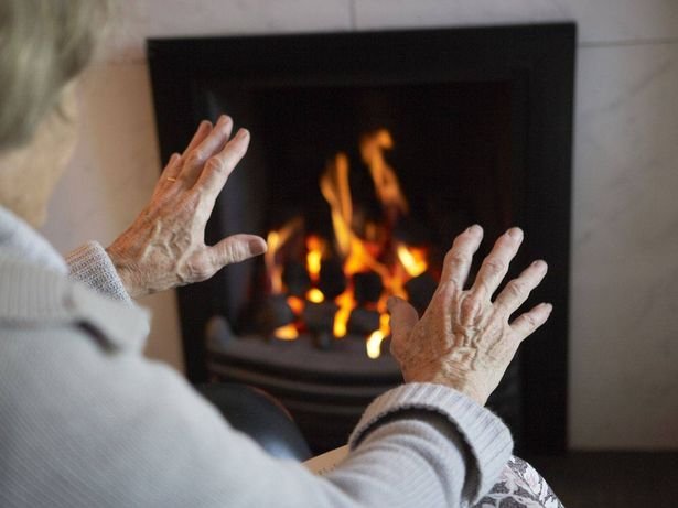 An older woman is heating her hands by an open fire 