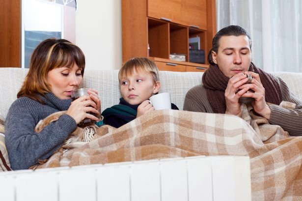 freezing family of three with cups of tea warming near warm radiator in home