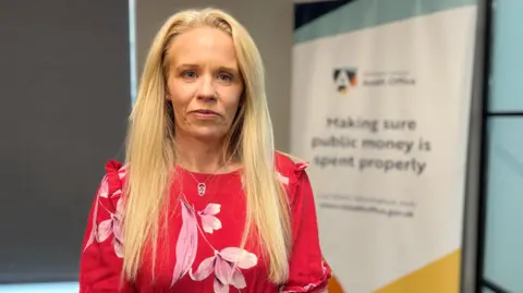 BBC A blonde woman in a red top with pink lilies over it