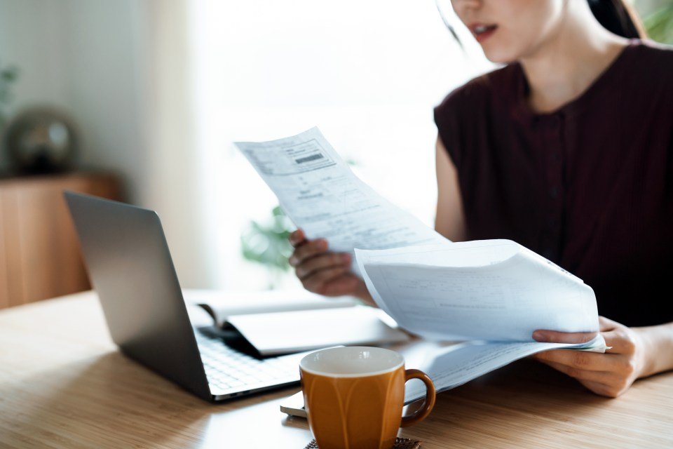 Woman reviewing financial documents with a laptop and coffee cup on the table.