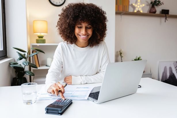  woman calculating expenses sitting on desk, using a calculator and laptop for her home finances