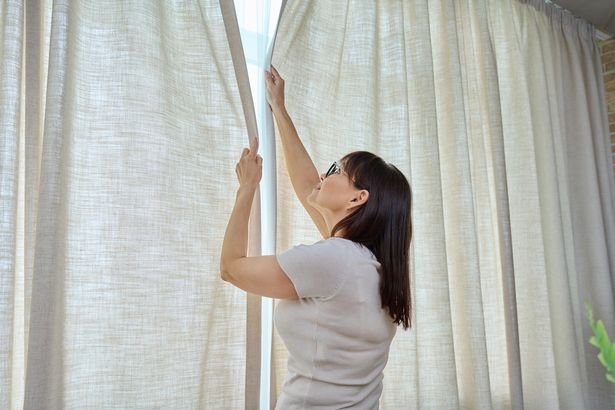 Back view, woman closes light linen curtains in the living room