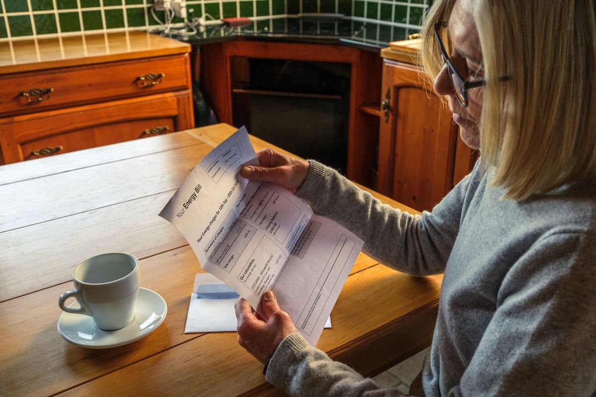 Senior woman sitting at the kitchen table anxiously reading an energy bill she just received through the post.