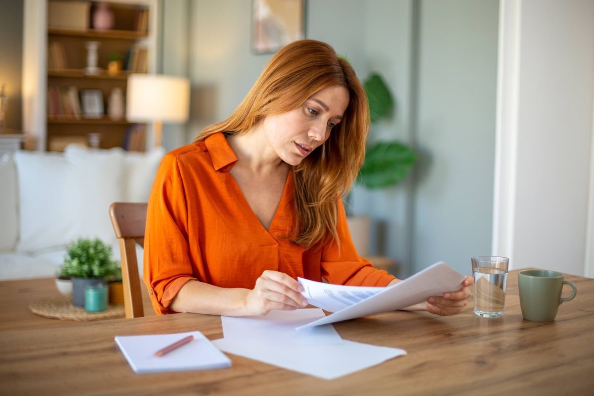 Serious woman sitting at home table reading the paper documents.
