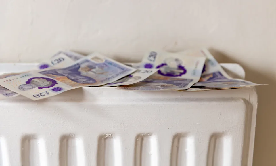 A loose pile of 20 pounds Sterling bank notes on top of a central heating radiator. A heating, utilities cost concept.