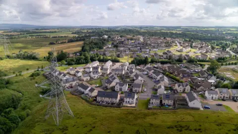 An aerial image of a new housing scheme with electricity pylons passing one side of the properties
