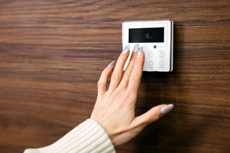 Hand is adjusting a digital thermostat mounted on a wooden wall, displaying temperature settings in a warm and inviting home setting