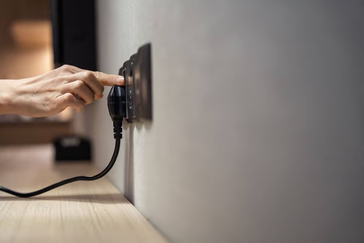 Hand plugging electrical cord into wall socket