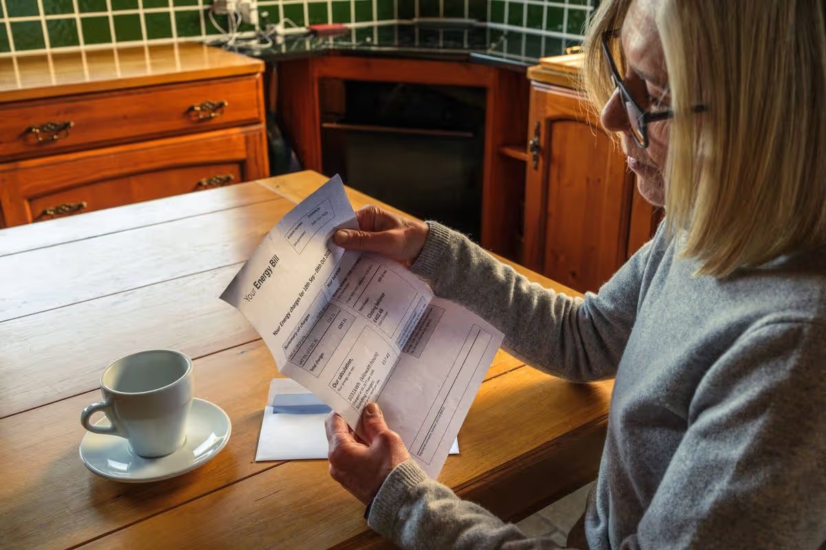 Senior woman sitting at the kitchen table anxiously reading an energy bill she just received through the post.