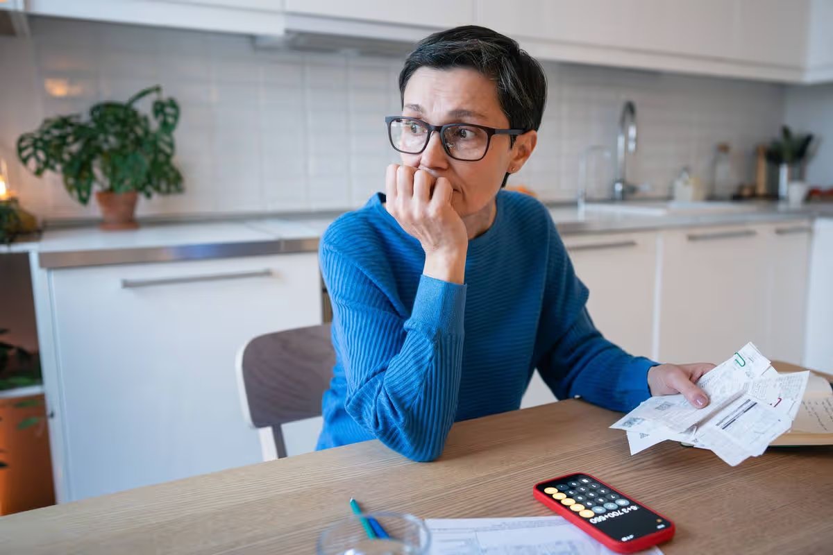 Stressed mature woman surrounded by bills and receipts, struggle with financial planning and debts. Balancing income, increased living costs and rising utility bills, budget pressure and crisis