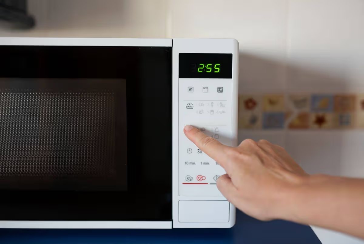 Hand pressing buttons on modern microwave oven with digital display