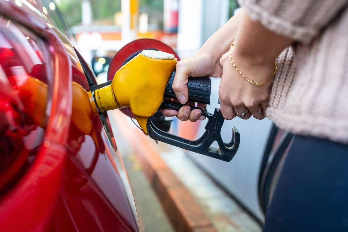 Person filling red car at gas pump, highlighting rising fuel costs and consumer strain as energy prices climb, affecting daily travel budgets and household expenses