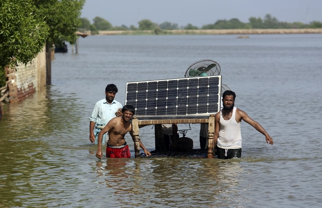 FILE - Men salvage a solar panel from their flooded home in Jaffarabad, Pakistan.