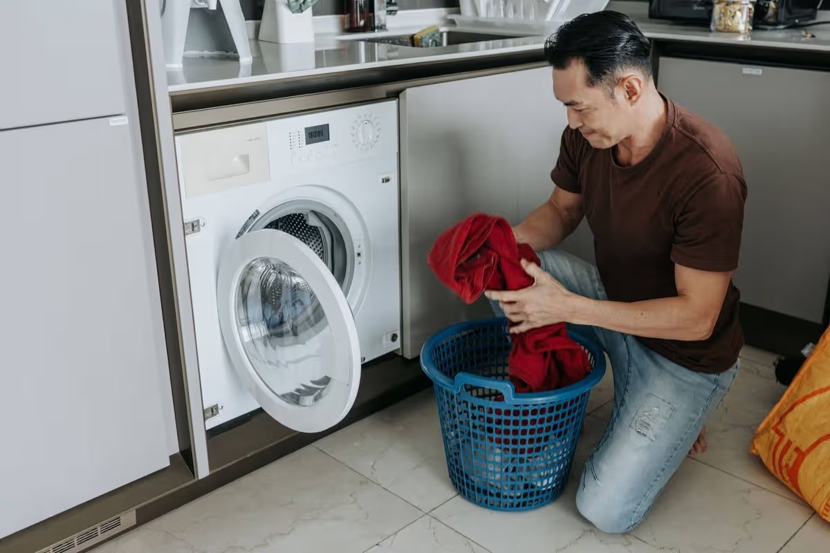Daily Home Chores Captured as a Mature Asian Man Loads Laundry Beside a Modern Washing Machine