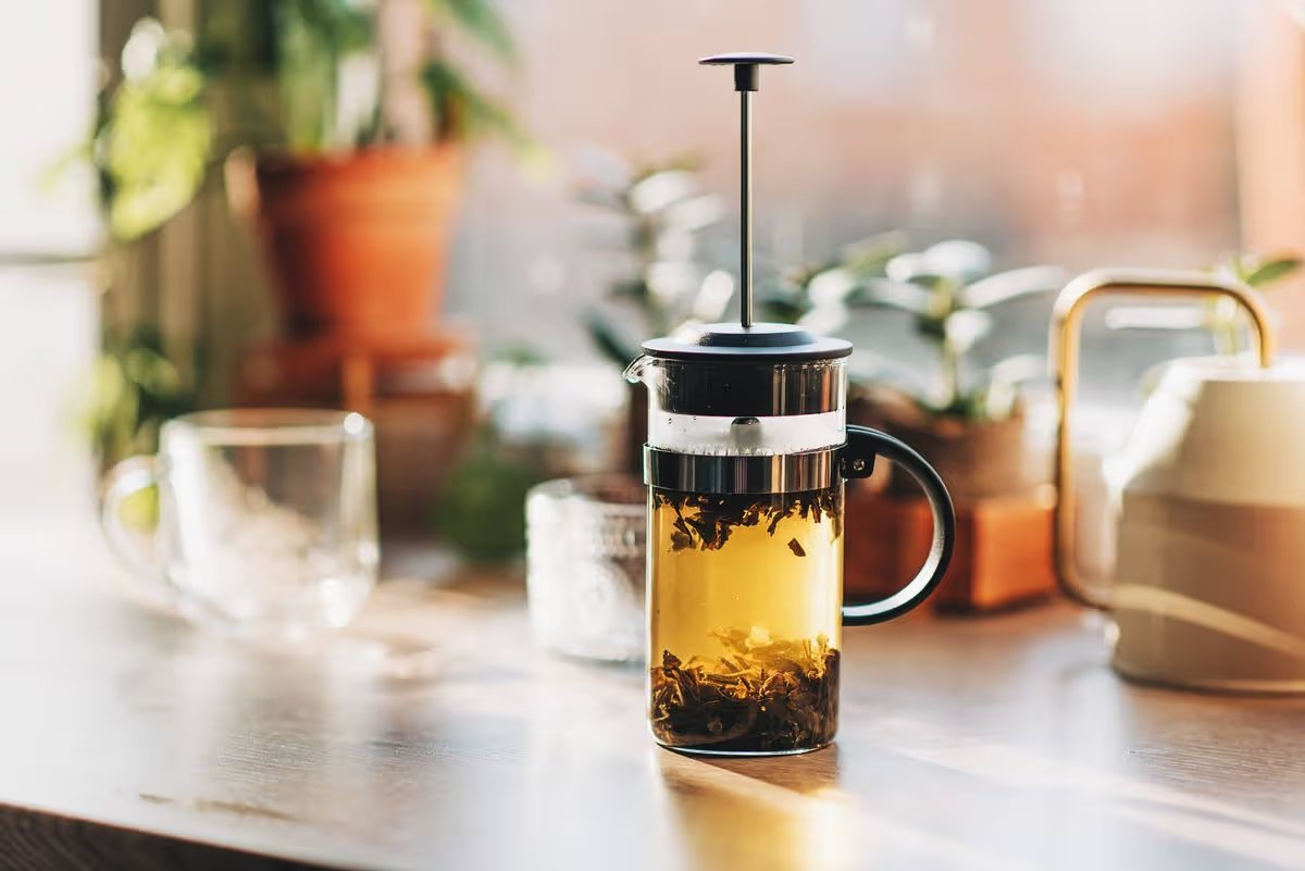 Green tea with fresh mint leaves brewed in a French press on a white table by the window.