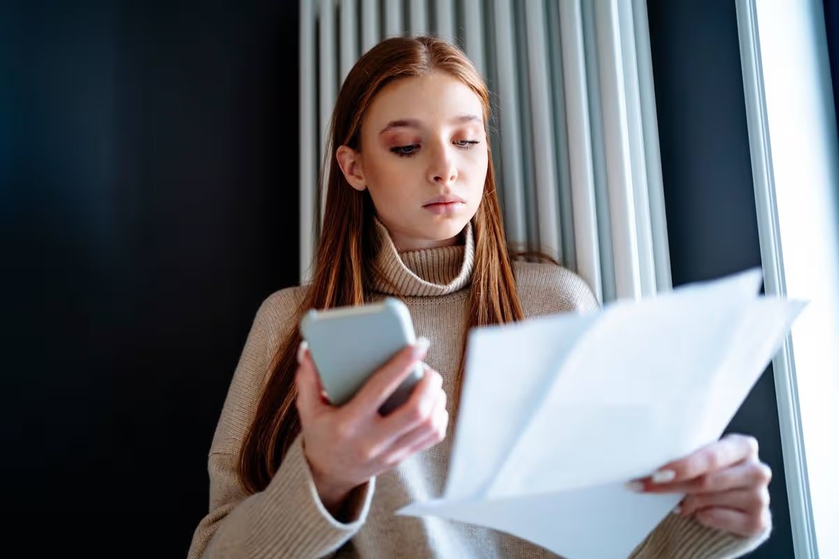 Teenage girl looking at energy bill standing by radiator heater