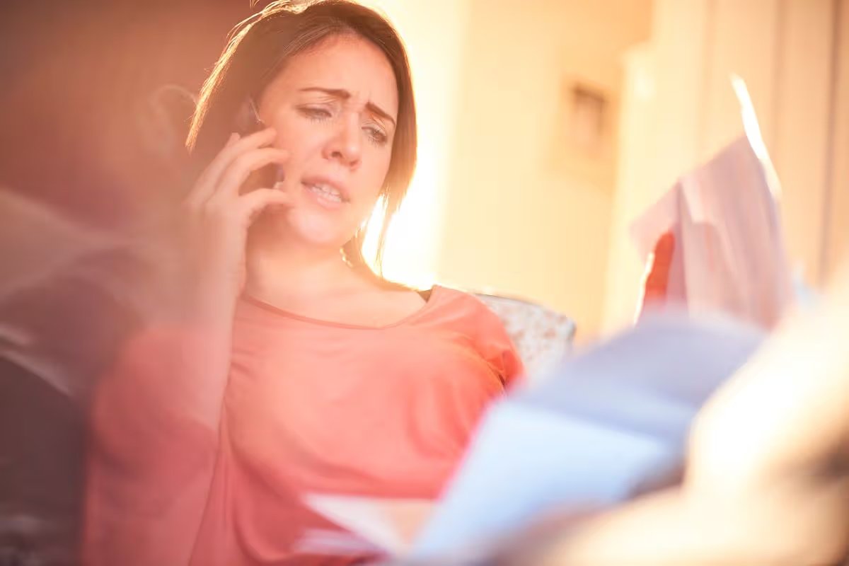 Woman looking worried while on phone and with bills in her hand 