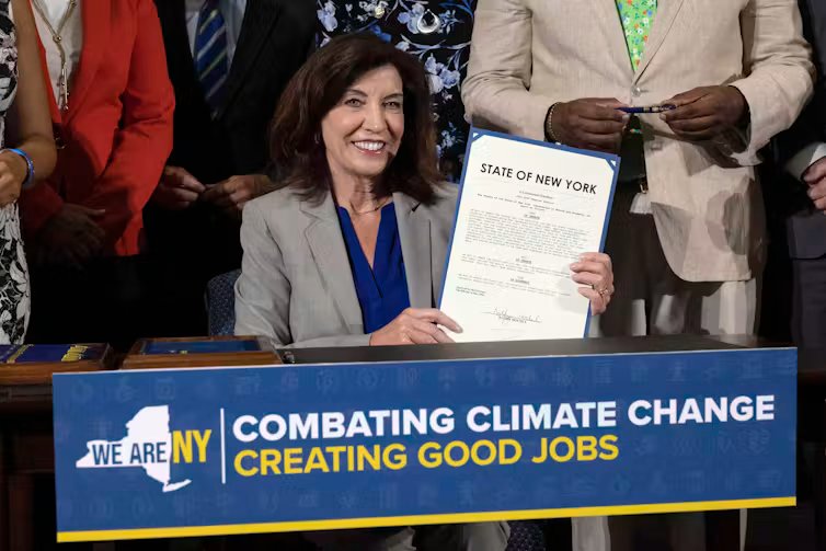 The governor smiles as she holds the signed legislation, sitting in front of a banner reading 'Combating climate change, creating good jobs'.