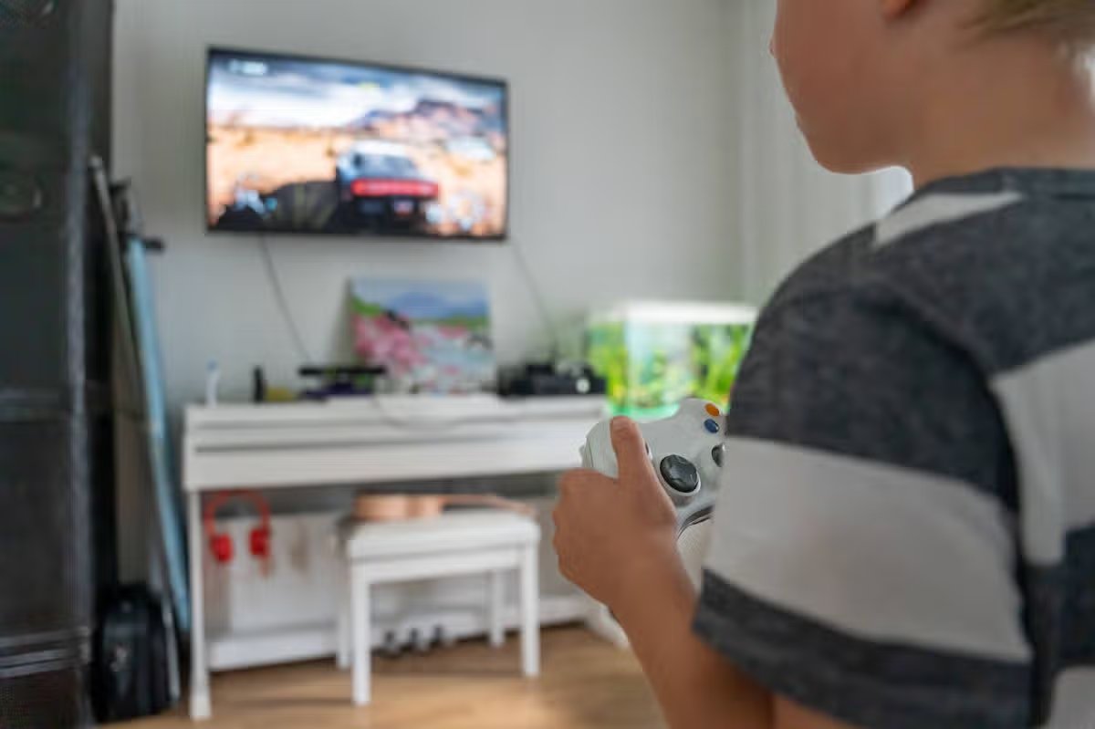 Boy with gamepad playing video games on tv at home. Close up faceless portrait over shoulder
