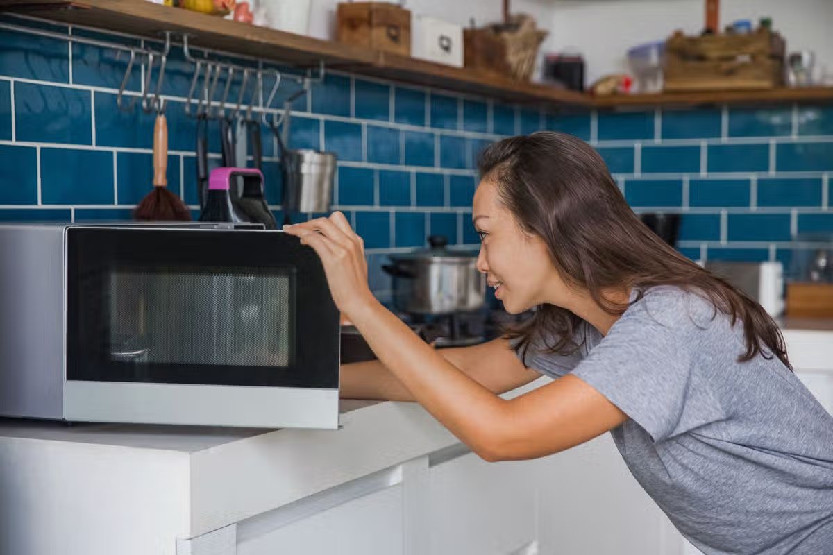Side shot of a woman opening her microwave to checking her meals that reheated.