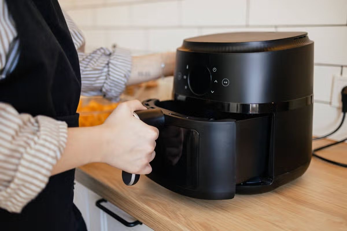 Close-up view of an unrecognisable woman putting a basket into a modern air fryer for cooking healthy meal